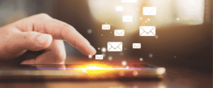Eine Hand berührt einen Tablet-Bildschirm, auf dem illustrierte E-Mail-Symbole nach oben schweben, die das Senden oder Empfangen von Nachrichten auf digitalem Wege symbolisieren. Warmes Licht leuchtet von dem Gerät in einem modernen, technikorientierten Umfeld - perfekt für die Kommunikation von Jobcoaching München.