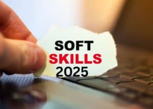 Eine Hand hält ein zerrissenes Stück Papier mit der Aufschrift SOFT SKILLS 2025 in fetten Buchstaben über einer Laptop-Tastatur.