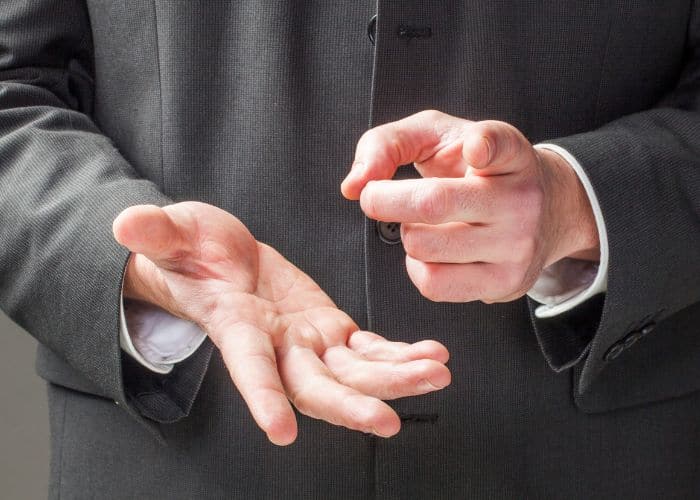 Eine Person im Anzug benutzt ihre Hände zum Zählen, wobei eine Hand offen ist und die andere auf etwas zeigt, um das Zählen anzudeuten oder einen Punkt während einer Diskussion zu betonen.