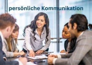 Eine Frau steht und deutet mit Gesten auf Dokumente auf einem Tisch, w&auml;hrend vier Kollegen sitzen und aufmerksam zuh&ouml;ren. &Uuml;ber ihnen erscheint der Text pers&ouml;nliche Kommunikation.