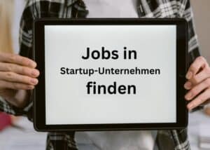 Eine Person, die ein Tablet in der Hand h&auml;lt, auf dem der deutsche Text &bdquo;Jobs in Startup-Unternehmen finden&ldquo; zu sehen ist, was so viel bedeutet wie &bdquo;Jobs in Start-up-Unternehmen finden&ldquo;. Die Person tr&auml;gt ein kariertes Hemd.